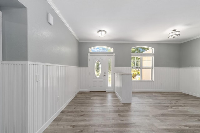 foyer entrance with ornamental molding, a wainscoted wall, and wood finished floors