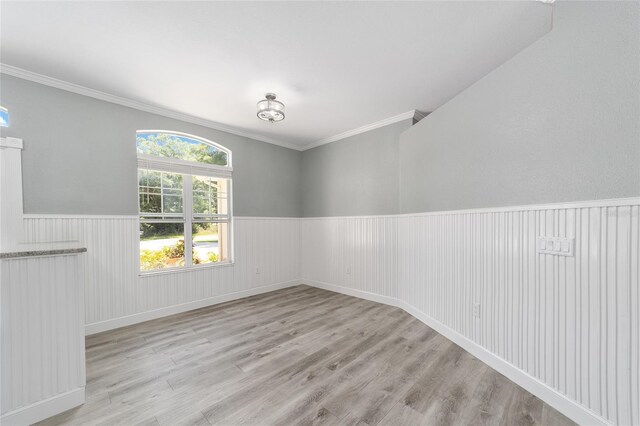 empty room with crown molding, wood finished floors, and wainscoting