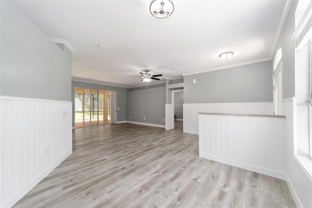 spare room with a wainscoted wall, ceiling fan, ornamental molding, and light wood-style flooring