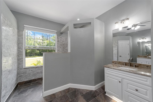 full bathroom featuring a walk in shower, two vanities, a sink, a ceiling fan, and baseboards