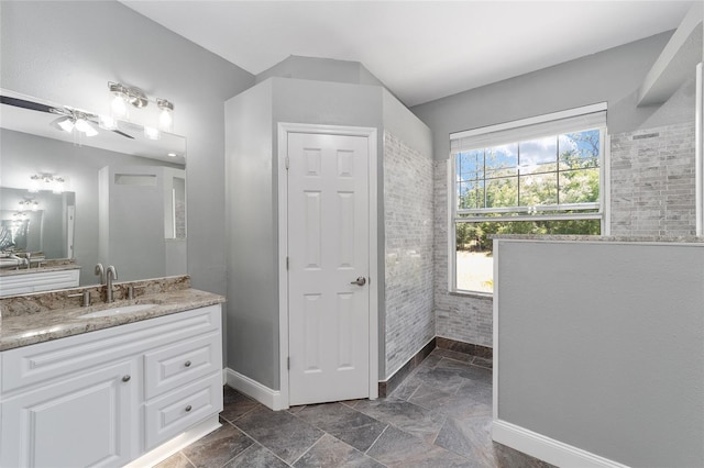 full bathroom featuring stone finish flooring, vanity, and baseboards