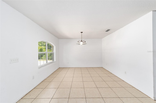 tiled spare room featuring a notable chandelier