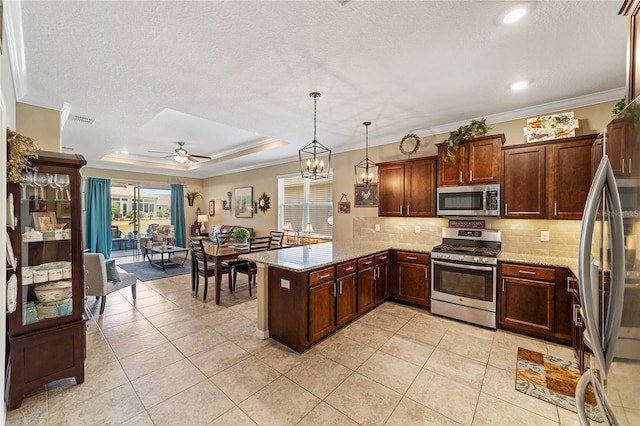 kitchen with ceiling fan with notable chandelier, hanging light fixtures, a tray ceiling, kitchen peninsula, and stainless steel appliances