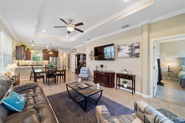 tiled living room with ceiling fan, ornamental molding, and a tray ceiling