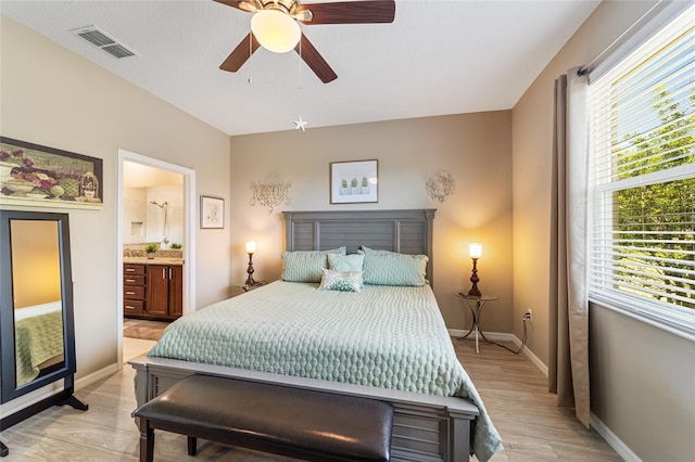 bedroom with multiple windows, light wood-type flooring, ensuite bath, and ceiling fan