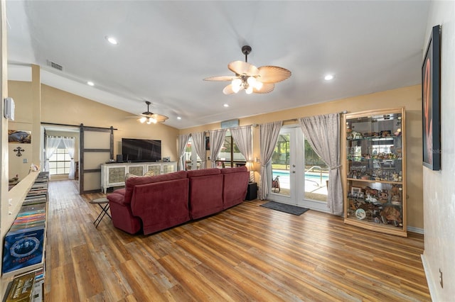 living room with a barn door, ceiling fan, french doors, hardwood / wood-style flooring, and lofted ceiling