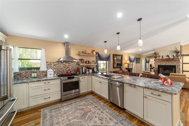 kitchen with stainless steel appliances, light stone counters, wall chimney exhaust hood, sink, and backsplash