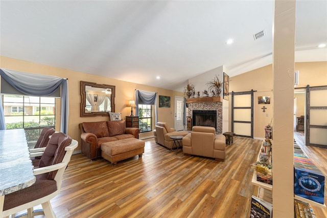 living room featuring wood-type flooring, a fireplace, vaulted ceiling, and a barn door