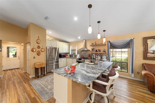 kitchen with wall chimney exhaust hood, decorative backsplash, lofted ceiling, a breakfast bar area, and appliances with stainless steel finishes