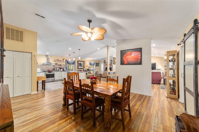 dining space with lofted ceiling, ceiling fan, a barn door, and light hardwood / wood-style flooring