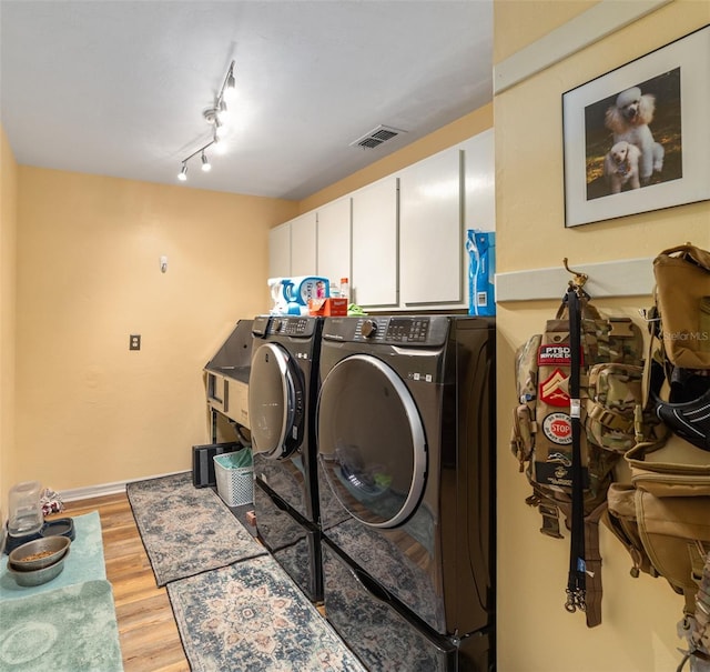 laundry area featuring washer and dryer, cabinets, light hardwood / wood-style floors, and rail lighting