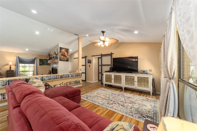 living room featuring vaulted ceiling, hardwood / wood-style floors, a barn door, a fireplace, and ceiling fan