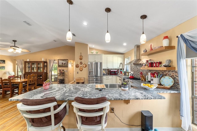 kitchen with island range hood, stainless steel refrigerator with ice dispenser, a kitchen bar, lofted ceiling, and backsplash