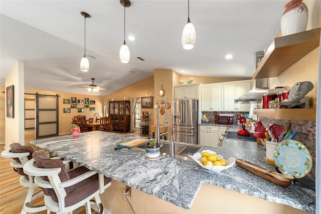 kitchen with vaulted ceiling, ceiling fan, backsplash, a barn door, and high end fridge