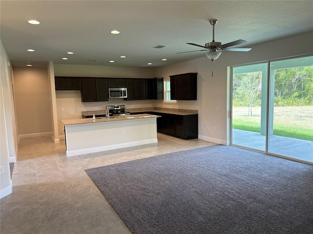 kitchen with light stone countertops, ceiling fan, an island with sink, light tile patterned flooring, and appliances with stainless steel finishes