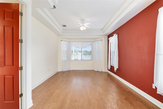 unfurnished room with light hardwood / wood-style floors, a raised ceiling, and ceiling fan