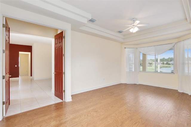 empty room featuring light wood-type flooring, a raised ceiling, and ceiling fan