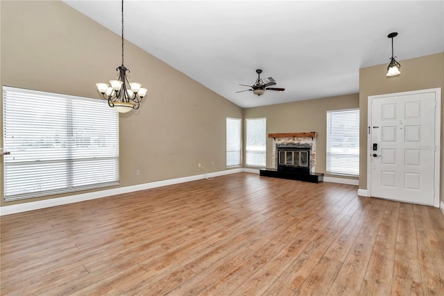 unfurnished living room with ceiling fan with notable chandelier, a stone fireplace, light wood-type flooring, and vaulted ceiling