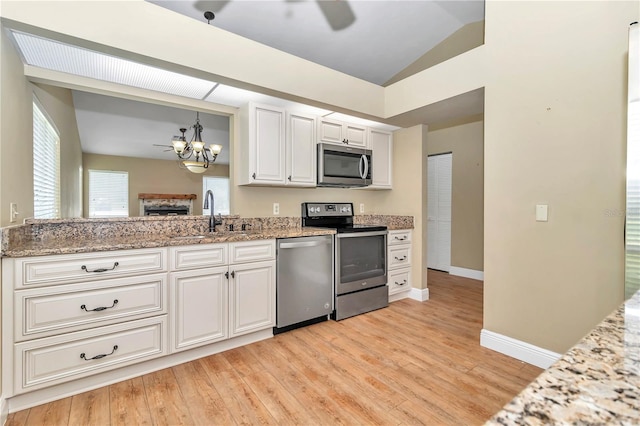 kitchen featuring appliances with stainless steel finishes, vaulted ceiling, sink, light hardwood / wood-style floors, and white cabinetry