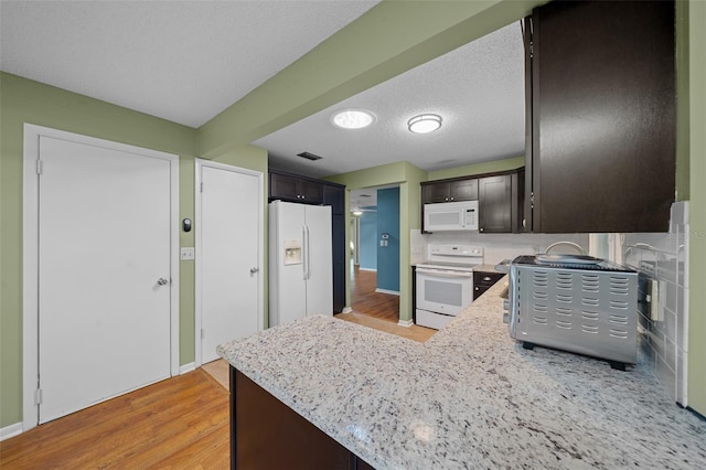 kitchen with a textured ceiling, dark brown cabinetry, white appliances, visible vents, and light wood-type flooring