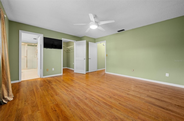 unfurnished bedroom with connected bathroom, light wood-style flooring, baseboards, and a textured ceiling