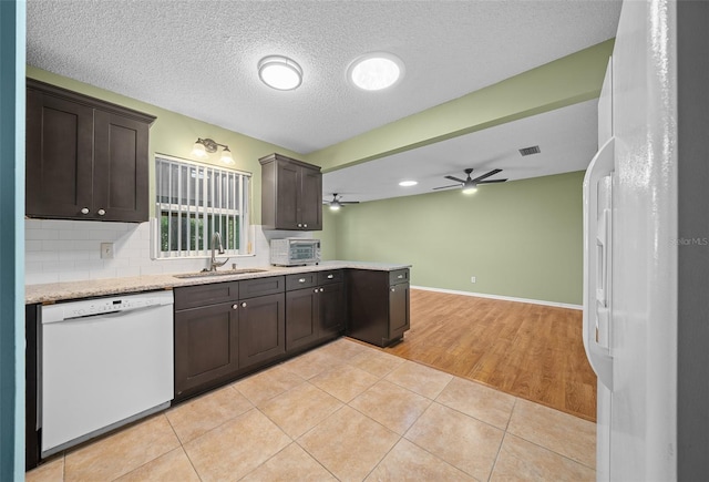 kitchen featuring light tile patterned floors, white appliances, a sink, dark brown cabinets, and backsplash