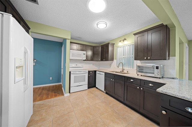 kitchen featuring dark brown cabinetry, white appliances, a toaster, light tile patterned floors, and a sink