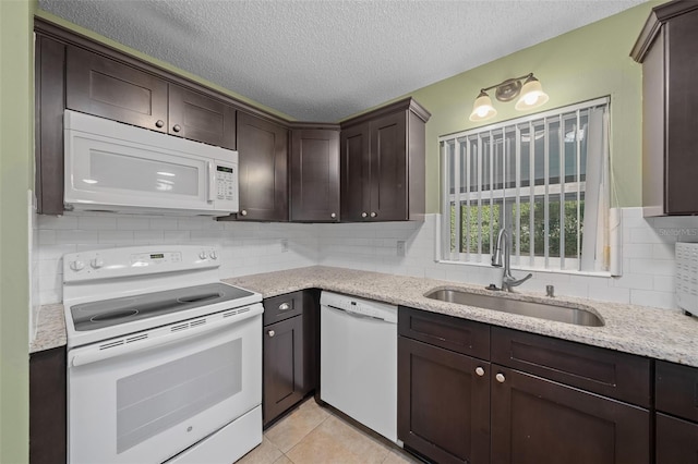 kitchen featuring light tile patterned flooring, a sink, dark brown cabinetry, light stone countertops, and white appliances