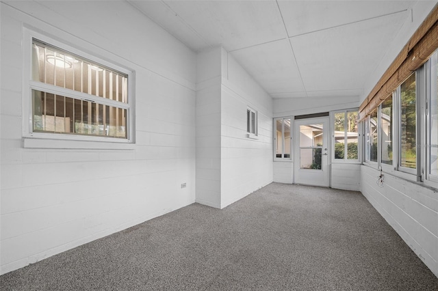 empty room with carpet floors, a sunroom, and concrete block wall