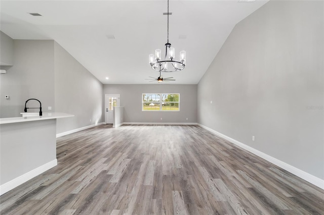 unfurnished living room with light wood-type flooring, lofted ceiling, sink, and ceiling fan with notable chandelier