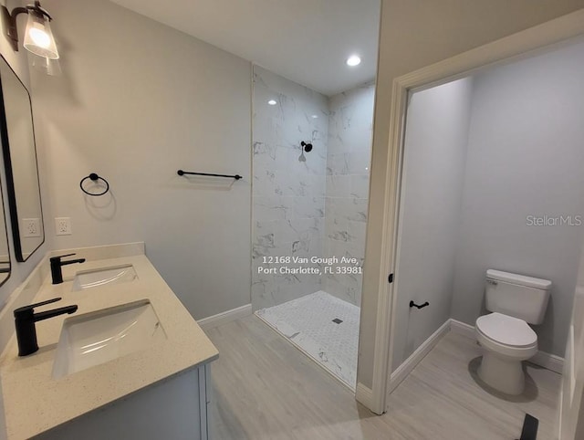 bathroom with hardwood / wood-style flooring, vanity, toilet, and a tile shower