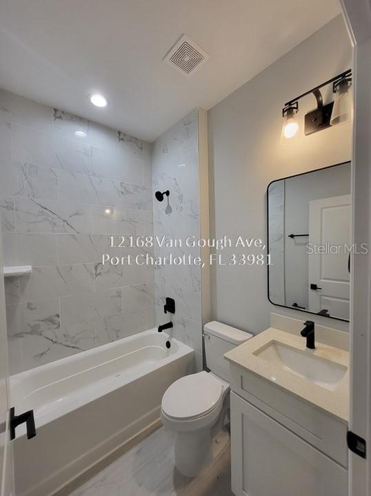 full bathroom with tiled shower / bath combo, toilet, and vanity