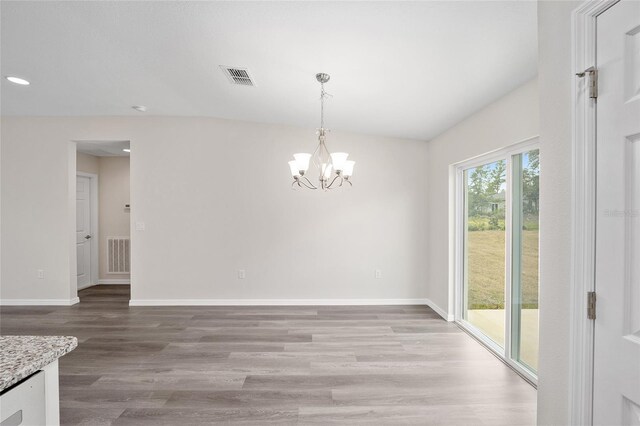 unfurnished dining area featuring wood-type flooring, vaulted ceiling, and a notable chandelier