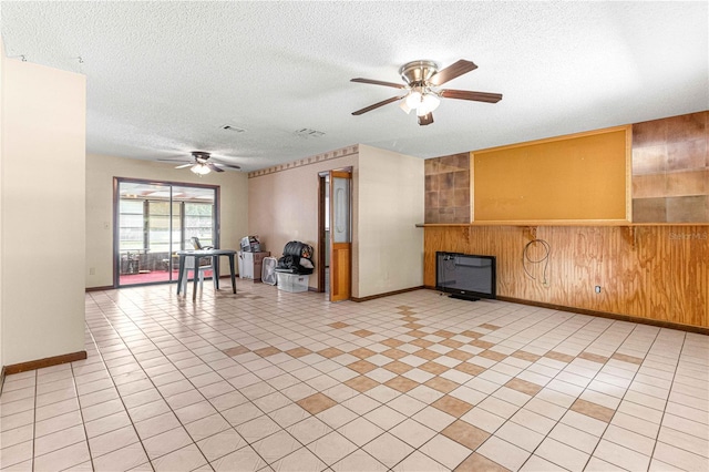 unfurnished living room with a textured ceiling, ceiling fan, and wooden walls