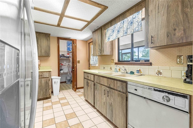 kitchen with sink, stainless steel fridge with ice dispenser, white dishwasher, a textured ceiling, and light tile patterned floors