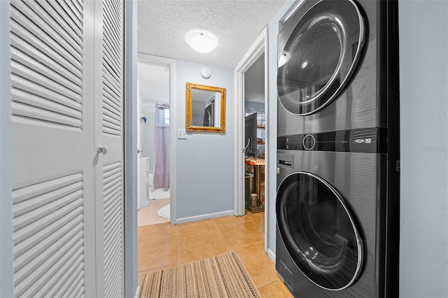 clothes washing area featuring stacked washer / dryer, light tile patterned floors, and a textured ceiling