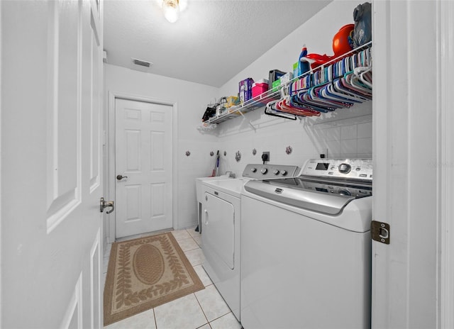 laundry room featuring visible vents, light tile patterned flooring, a textured ceiling, separate washer and dryer, and laundry area