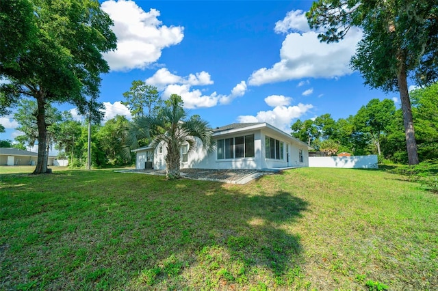 rear view of property with stucco siding, fence, and a lawn