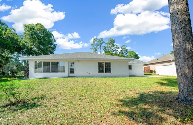 back of house featuring a lawn, fence, and stucco siding