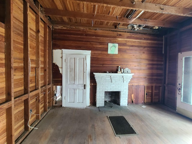 unfurnished living room featuring hardwood / wood-style floors, beam ceiling, a fireplace, and wooden walls