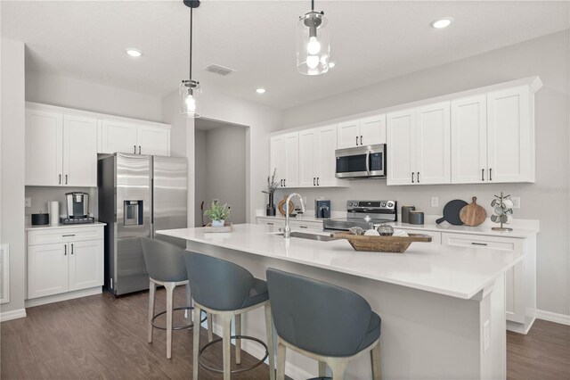 kitchen featuring white cabinets, appliances with stainless steel finishes, decorative light fixtures, and a center island with sink