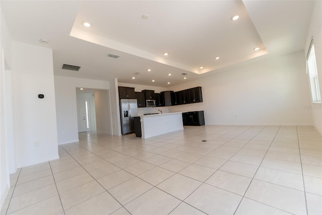 unfurnished living room with sink, a tray ceiling, and light tile patterned floors