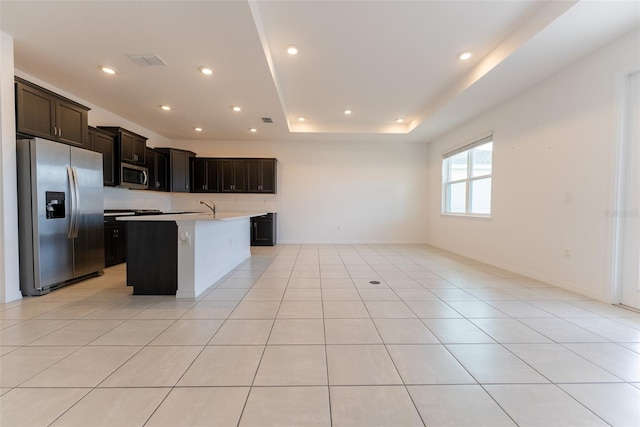 kitchen featuring light tile patterned floors, appliances with stainless steel finishes, a tray ceiling, and a center island with sink