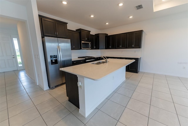 kitchen with a center island with sink, light tile patterned floors, light stone countertops, sink, and stainless steel appliances