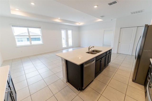 kitchen with sink, an island with sink, a raised ceiling, stainless steel appliances, and light tile patterned floors