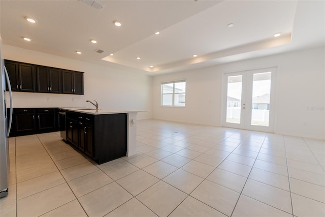 kitchen featuring sink, french doors, a tray ceiling, and an island with sink