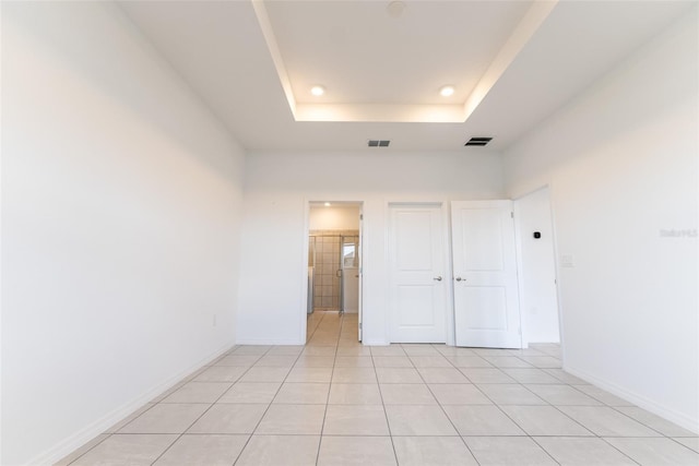 unfurnished bedroom featuring ensuite bathroom, a tray ceiling, and light tile patterned floors