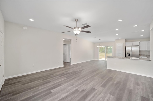 unfurnished living room featuring ceiling fan with notable chandelier and hardwood / wood-style flooring