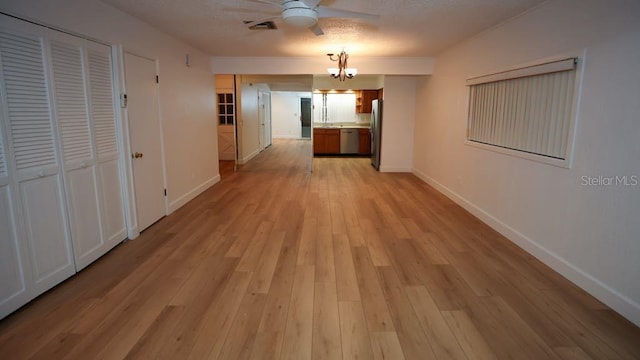 hallway with light hardwood / wood-style floors, a textured ceiling, and a notable chandelier