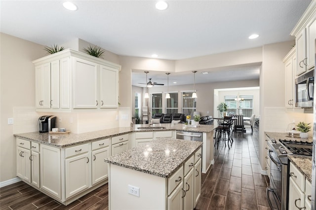 kitchen with ceiling fan, appliances with stainless steel finishes, decorative light fixtures, dark hardwood / wood-style flooring, and kitchen peninsula